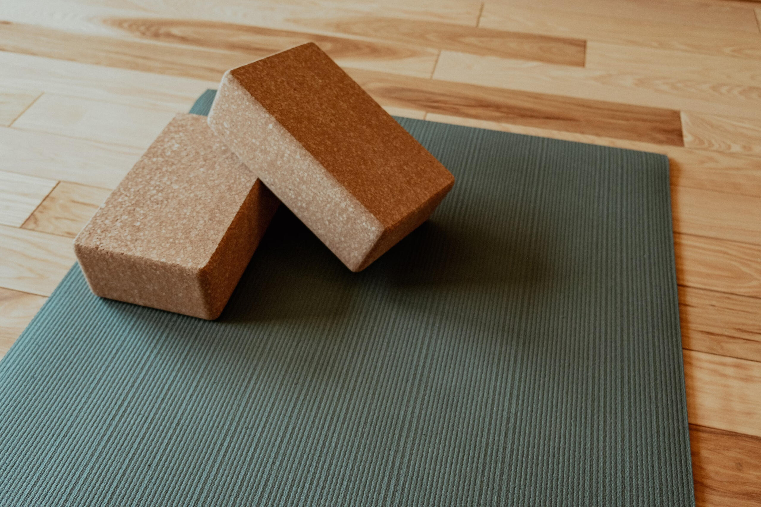 Cork yoga blocks resting on a light teal yoga mat on a softly lit bamboo studio floor.